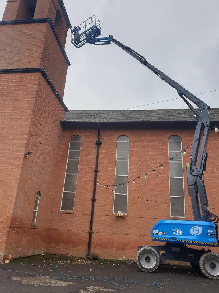 Cherry picker reaching a red-brick church tower for high-level cleaning