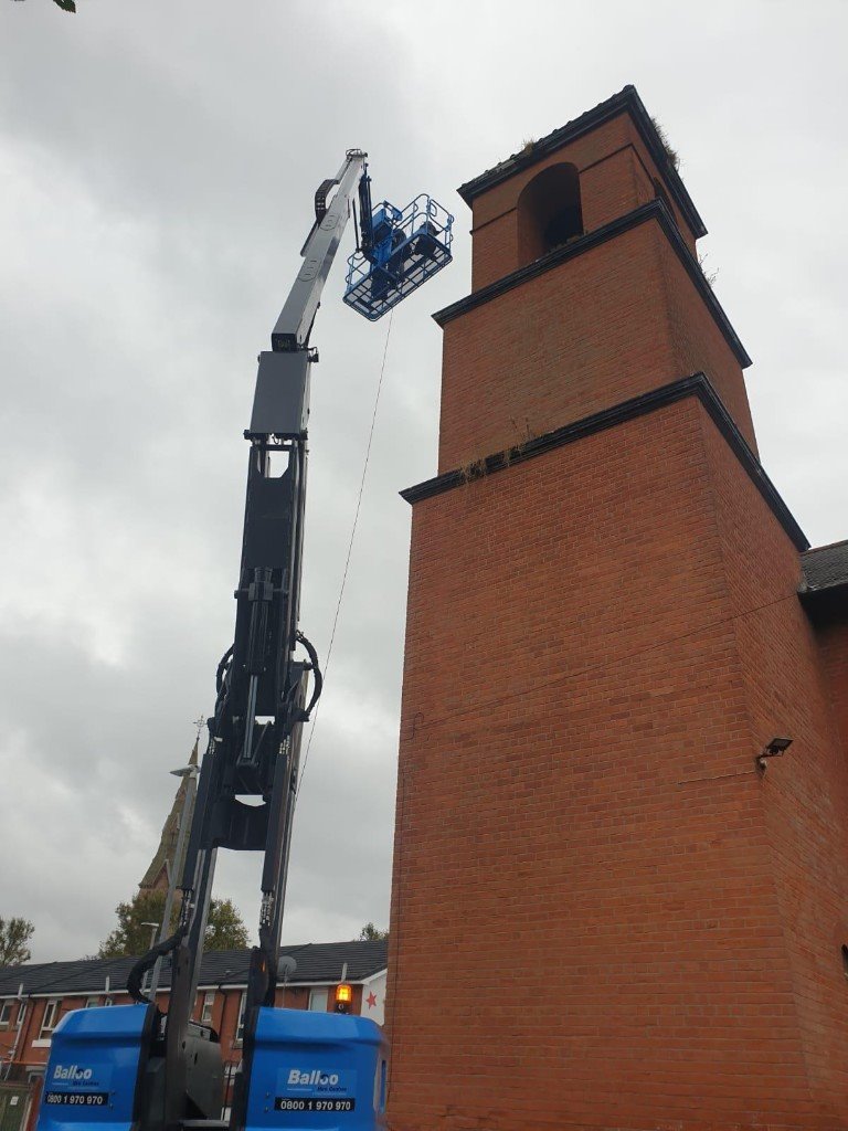 Boom lift extended to the top of a tall brick church tower
