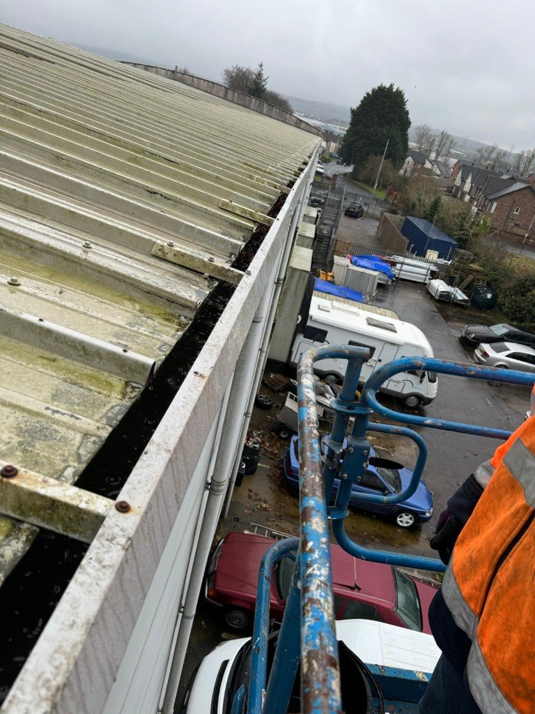 Clogged industrial gutter and mossy corrugated roof seen from a cherry picker