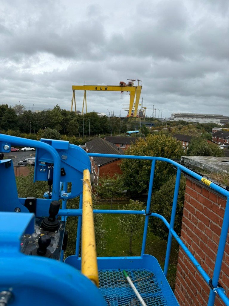 Cherry picker basket above a Belfast street, Harland and Wolff cranes in the distance