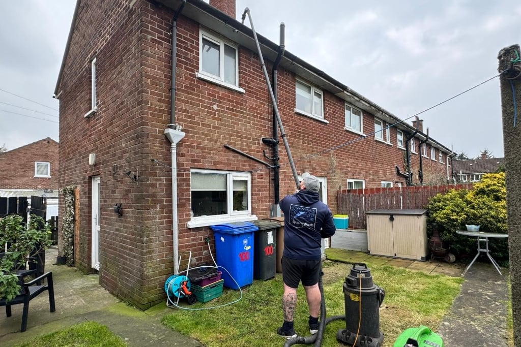 QuickWash NI clearing a house gutter with a vacuum pole from the ground, collection drums on the lawn